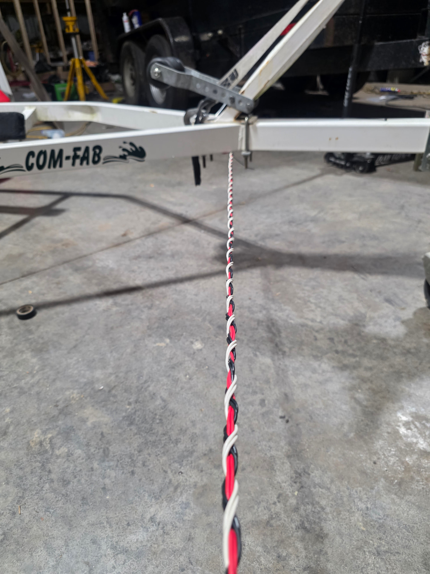 Trailer wires twisted and run along the underside of a white Com-Fab trailer frame during a wiring job